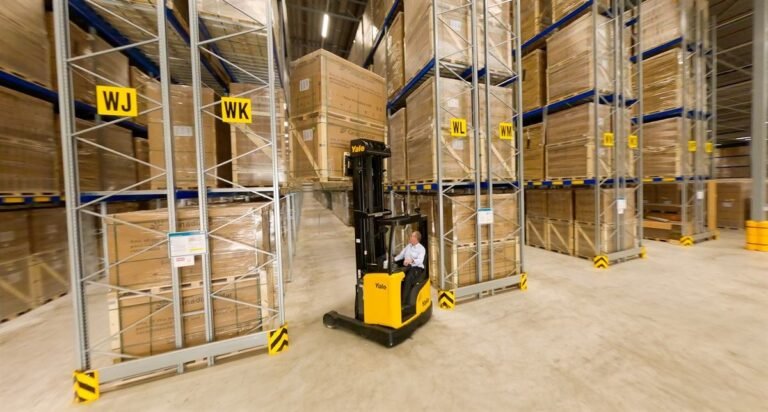 Employee on a reach truck between high warehouse racks with pallets